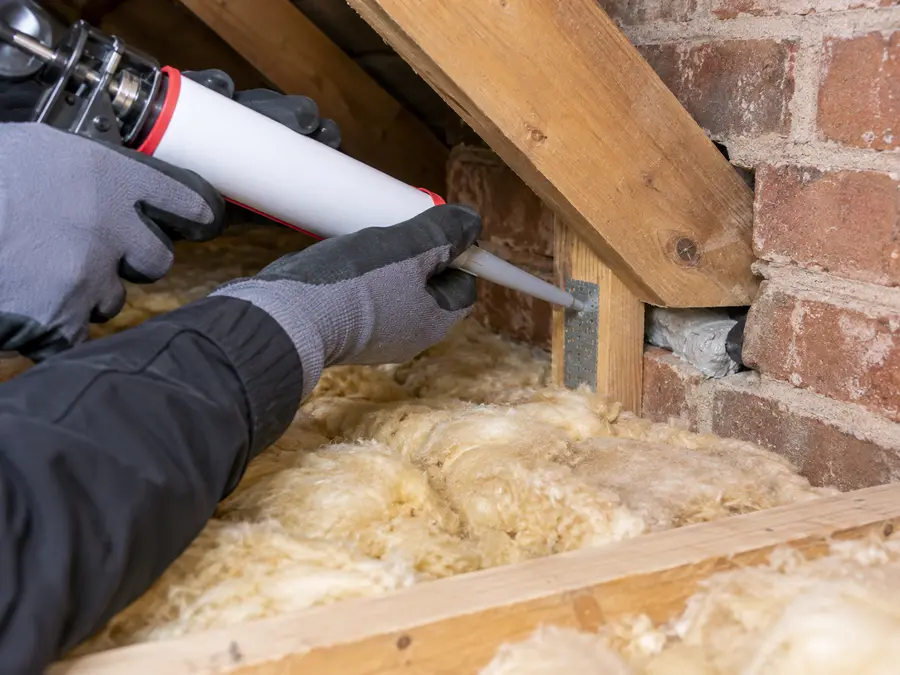 Pest control technician sealing a rodent entry gap in a loft